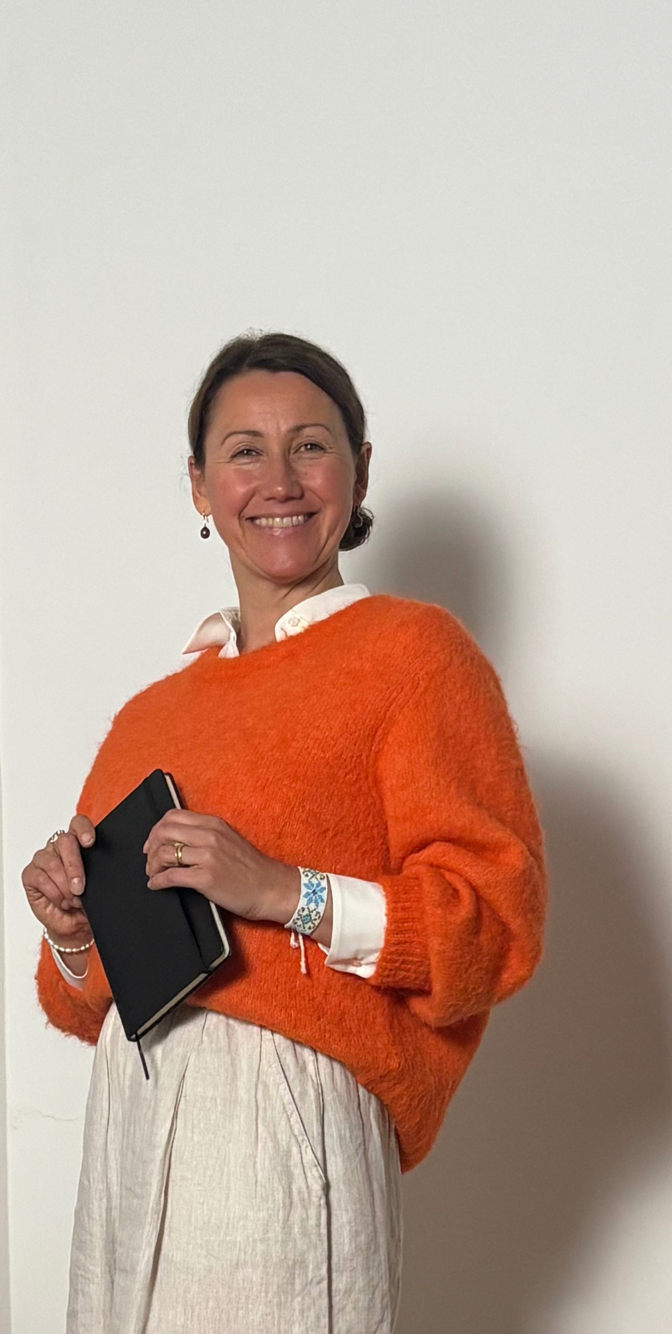 Irina Schmidt mit Notizbuch, orangefarbener Pullover, lachend