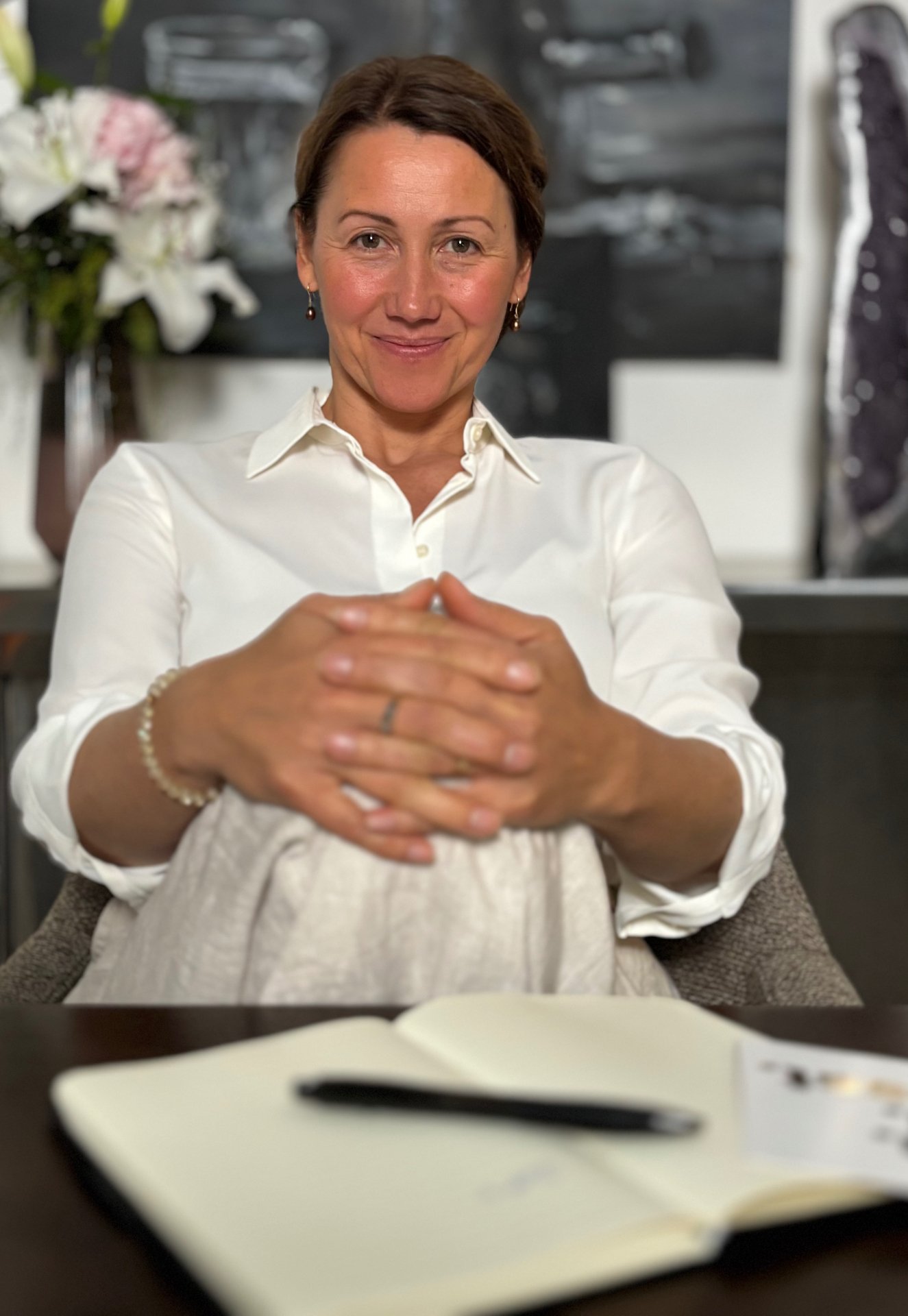 Irina Schmidt am Tisch, weißes Hemd, Hände gefaltet, Amethyst im Hintergrund