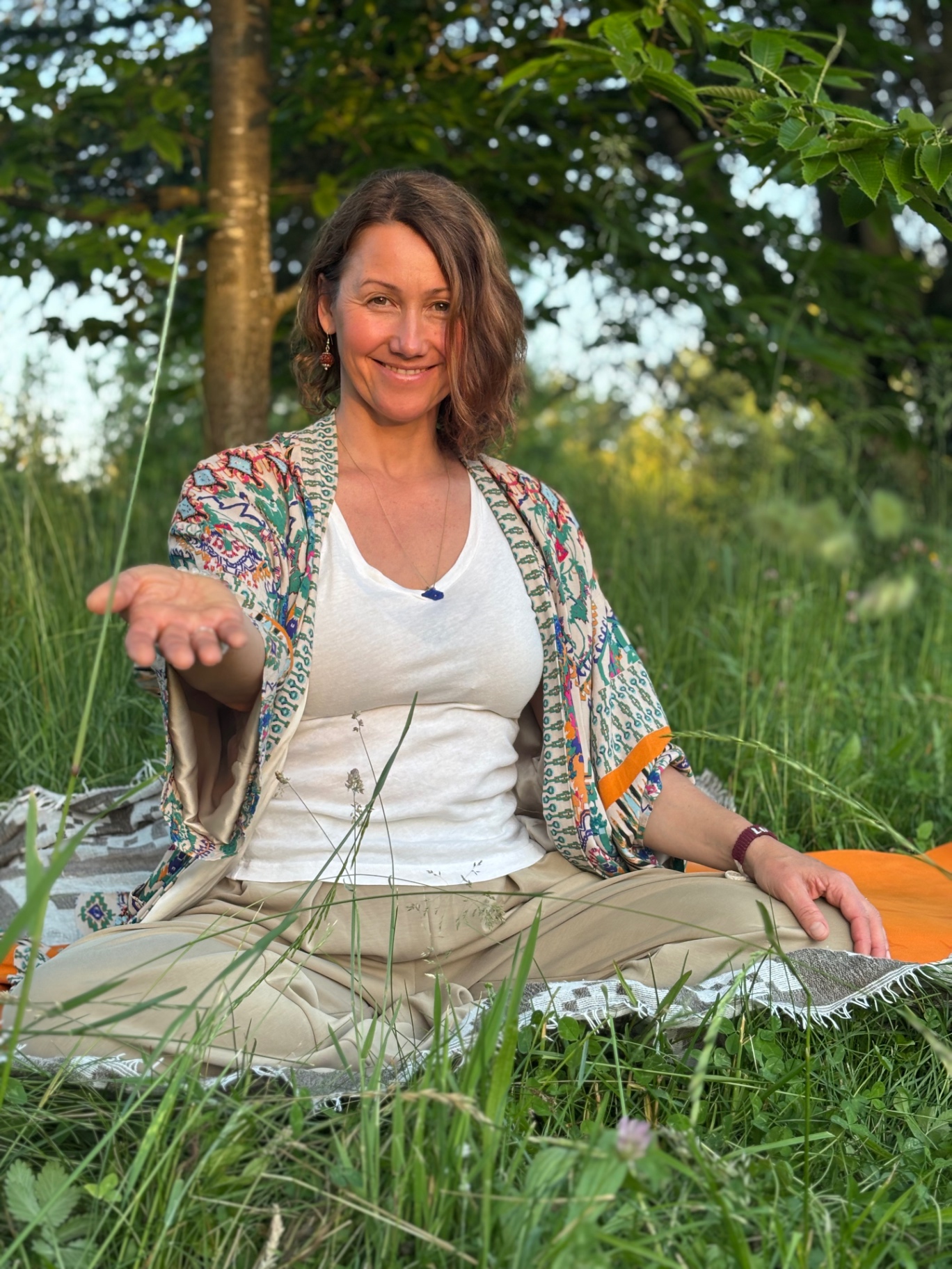 Irina Schmidt im Schneidersitz auf einer Wiese, einladende Geste